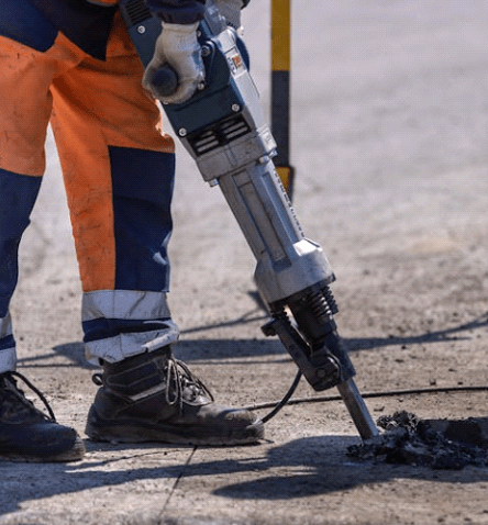 pracownik budowy który kuje beton przy pomocy młota pneumatycznego