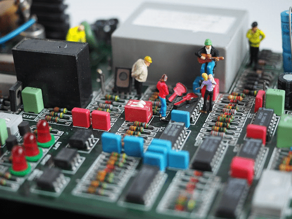 Miniaturowe figurki pracowników na płycie głównej elektroniki symbolizujące zespół IT, zarządzanie projektami i współpracę w technologii.